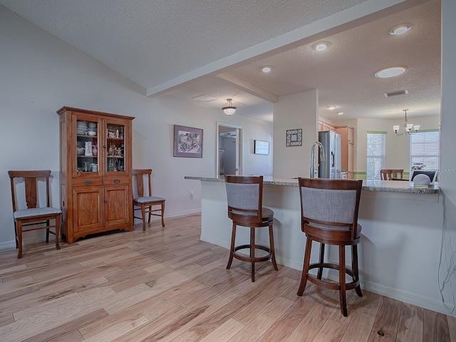 kitchen with decorative light fixtures, light hardwood / wood-style flooring, a notable chandelier, and kitchen peninsula