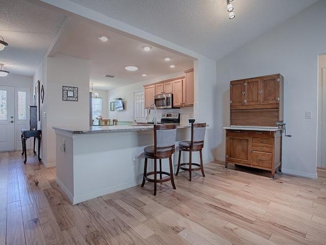 kitchen with light hardwood / wood-style flooring, appliances with stainless steel finishes, a kitchen breakfast bar, a textured ceiling, and kitchen peninsula