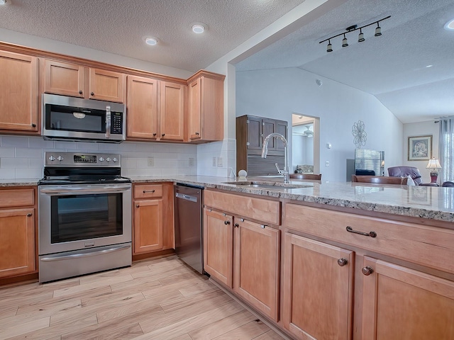 kitchen featuring vaulted ceiling, appliances with stainless steel finishes, sink, backsplash, and a textured ceiling