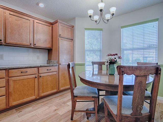 dining area with a notable chandelier, a textured ceiling, and light wood-type flooring