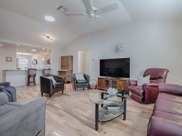 living room with lofted ceiling, ceiling fan with notable chandelier, light hardwood / wood-style flooring, and a textured ceiling