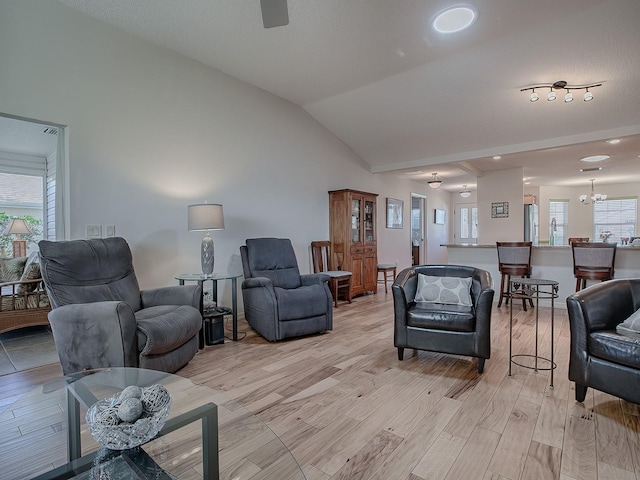 living room with lofted ceiling, ceiling fan with notable chandelier, and light hardwood / wood-style flooring