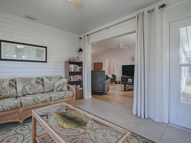 living room with plenty of natural light, tile patterned floors, ceiling fan, and wood walls