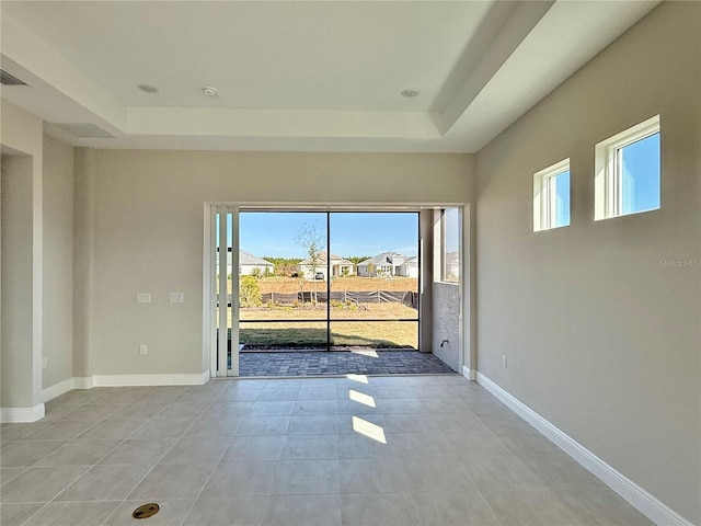 tiled empty room with a tray ceiling and a wealth of natural light