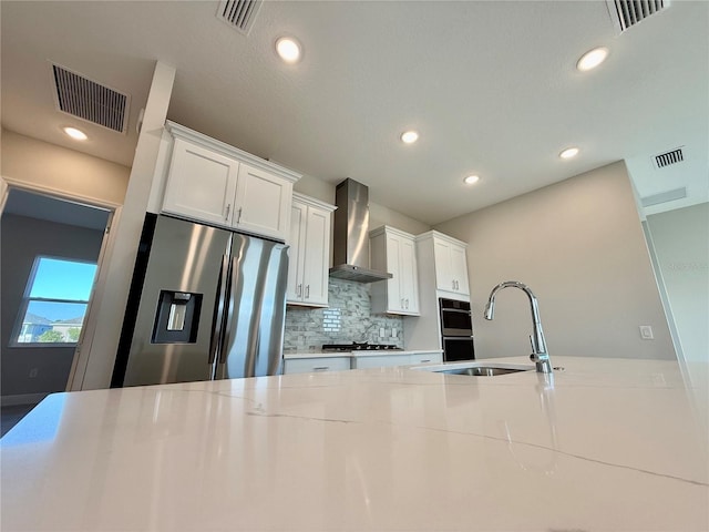 kitchen with white cabinetry, sink, light stone countertops, wall chimney range hood, and appliances with stainless steel finishes