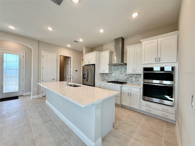 kitchen with a center island with sink, sink, wall chimney exhaust hood, appliances with stainless steel finishes, and white cabinetry