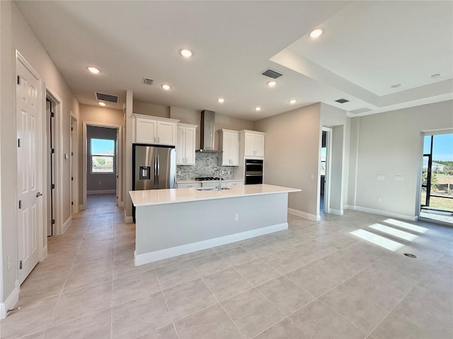 kitchen with white cabinets, wall chimney exhaust hood, stainless steel fridge with ice dispenser, and a kitchen island with sink