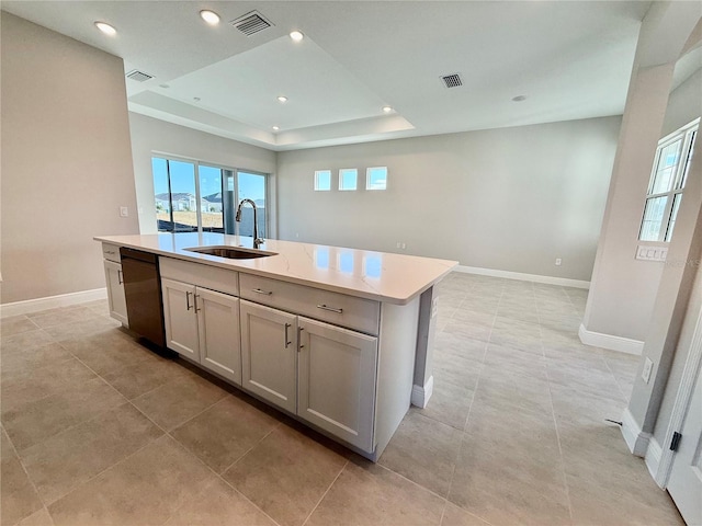 kitchen featuring dishwasher, sink, a raised ceiling, gray cabinets, and a kitchen island with sink