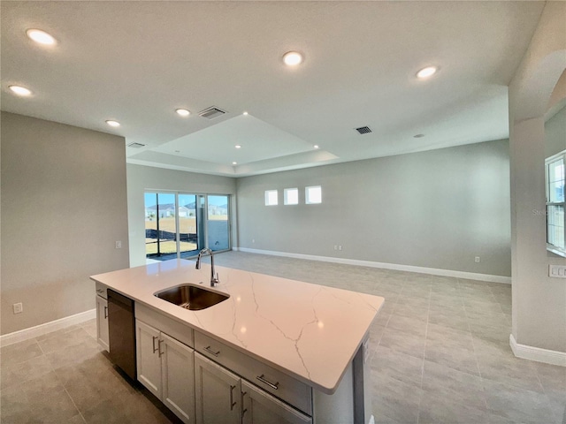 kitchen featuring light stone countertops, sink, stainless steel dishwasher, a tray ceiling, and a center island with sink