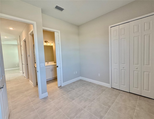 unfurnished bedroom with connected bathroom, a closet, and light tile patterned flooring