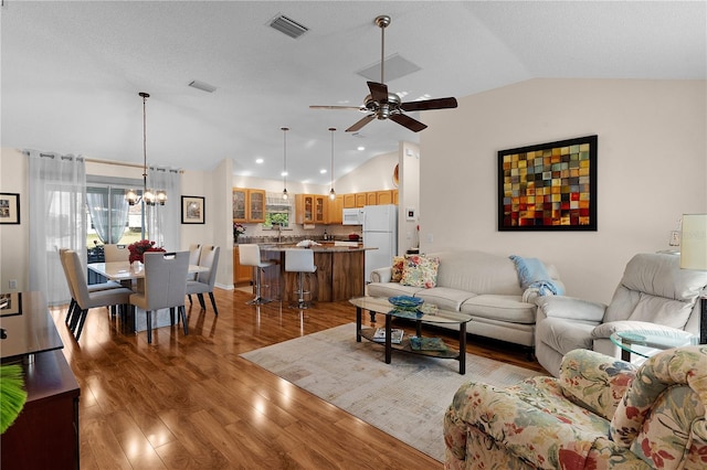 living room with ceiling fan with notable chandelier, light hardwood / wood-style floors, a healthy amount of sunlight, and vaulted ceiling