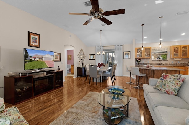 living room featuring ceiling fan with notable chandelier, wood-type flooring, and lofted ceiling