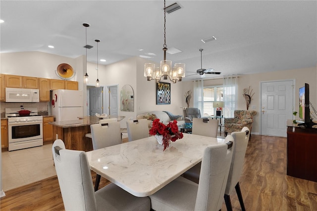 dining room with ceiling fan, vaulted ceiling, and light hardwood / wood-style flooring