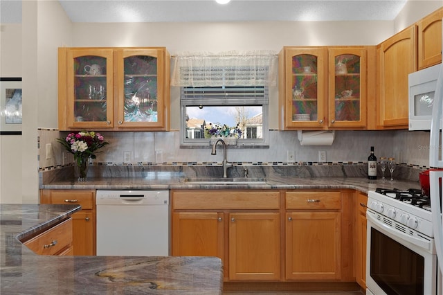 kitchen featuring sink, backsplash, dark stone counters, and white appliances