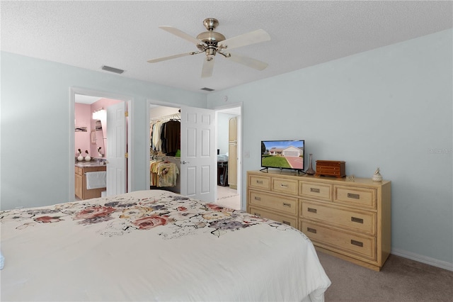 bedroom featuring a spacious closet, a textured ceiling, light carpet, a closet, and ceiling fan