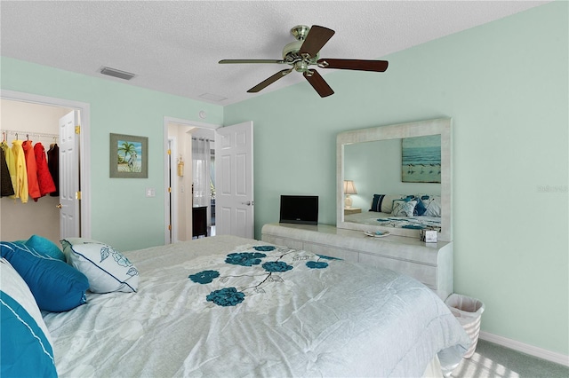 bedroom featuring a textured ceiling, a walk in closet, carpet floors, a closet, and ceiling fan