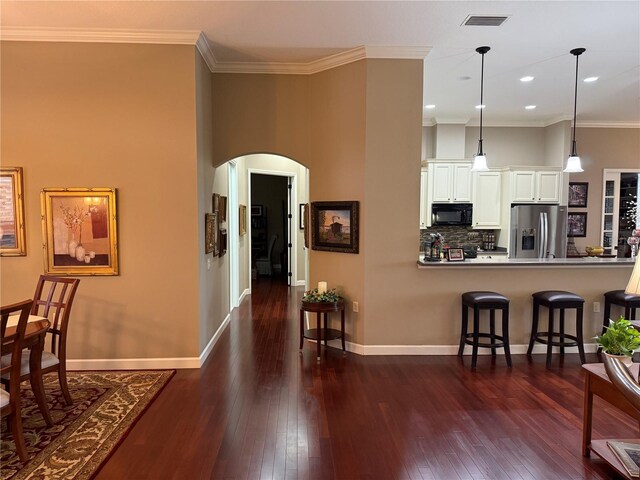 kitchen featuring stainless steel fridge, ornamental molding, white cabinetry, hanging light fixtures, and a breakfast bar area