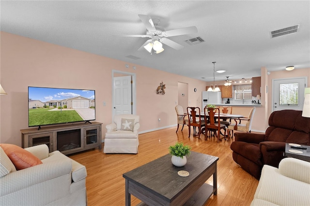 living room with ceiling fan with notable chandelier, light wood-type flooring, and a textured ceiling