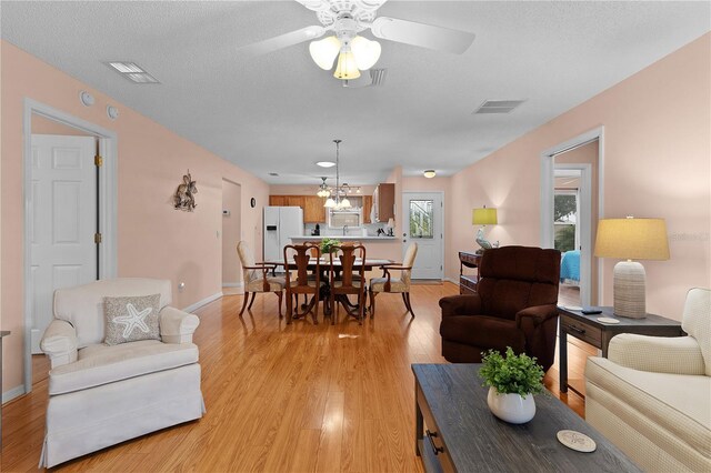 living room featuring ceiling fan with notable chandelier, light wood-type flooring, and a textured ceiling