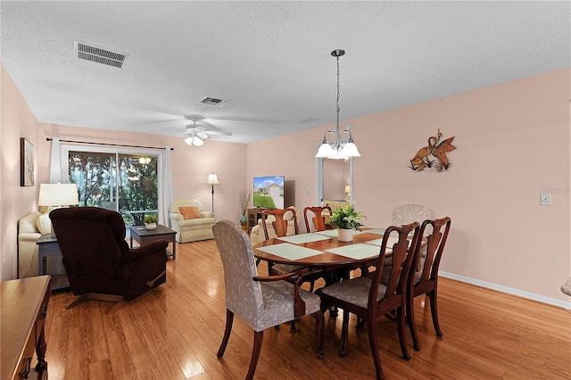 dining area featuring a textured ceiling, light hardwood / wood-style flooring, and ceiling fan with notable chandelier