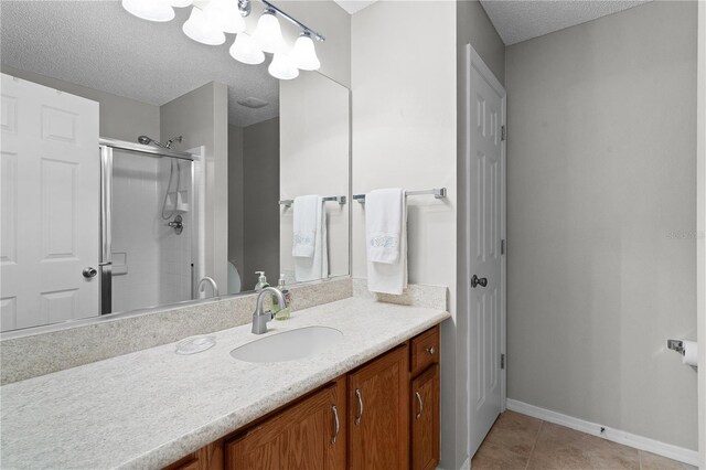 bathroom with tile patterned floors, vanity, a shower with door, and a textured ceiling