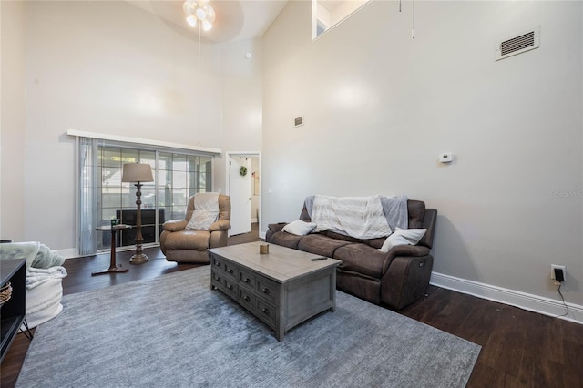 living room featuring dark wood-type flooring, ceiling fan, and a high ceiling