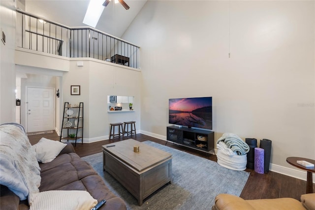 living room with a skylight, dark wood-type flooring, high vaulted ceiling, and ceiling fan