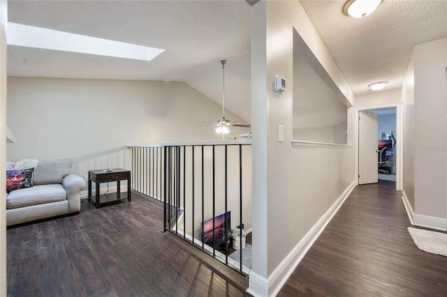 hall with dark hardwood / wood-style flooring, a textured ceiling, and lofted ceiling with skylight