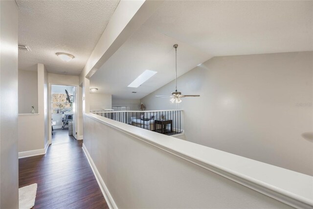 hall featuring dark hardwood / wood-style floors, vaulted ceiling with skylight, and a textured ceiling