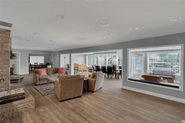 living room featuring a brick fireplace, a textured ceiling, a healthy amount of sunlight, and light wood-type flooring