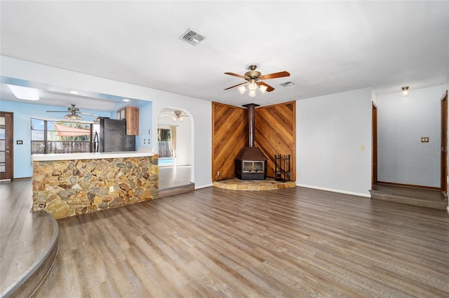 unfurnished living room featuring wood-type flooring, ceiling fan, and a wood stove