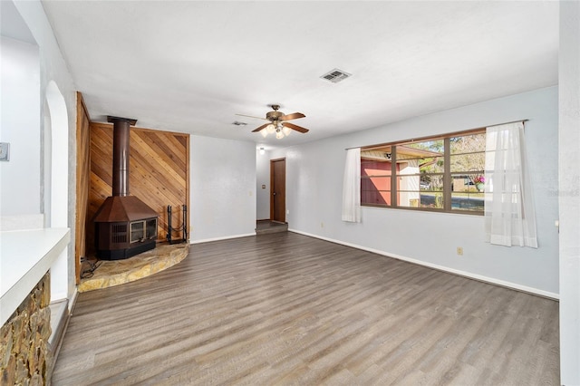 unfurnished living room featuring hardwood / wood-style flooring, wood walls, ceiling fan, and a wood stove