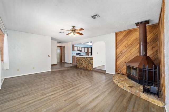 unfurnished living room featuring wood-type flooring, a wood stove, and ceiling fan
