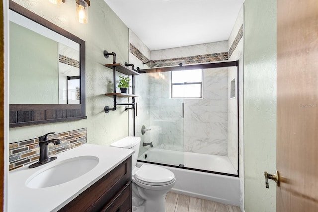 full bathroom featuring backsplash, bath / shower combo with glass door, vanity, wood-type flooring, and toilet