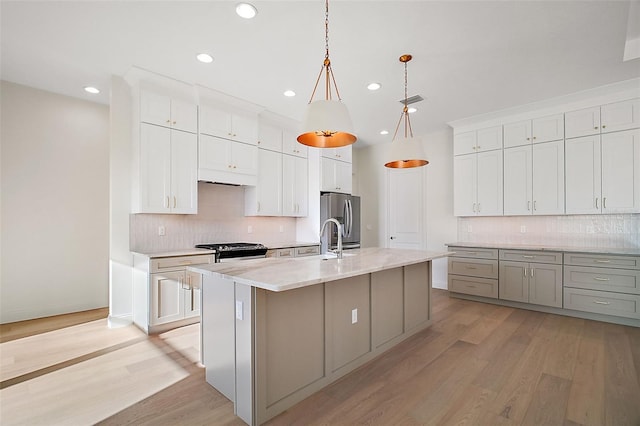 kitchen with light hardwood / wood-style floors, white cabinetry, a kitchen island with sink, pendant lighting, and stainless steel appliances