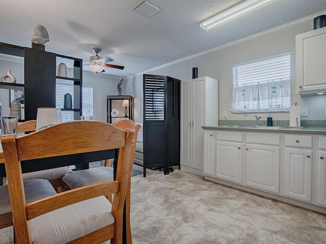 kitchen with a textured ceiling, white cabinetry, ceiling fan, and crown molding