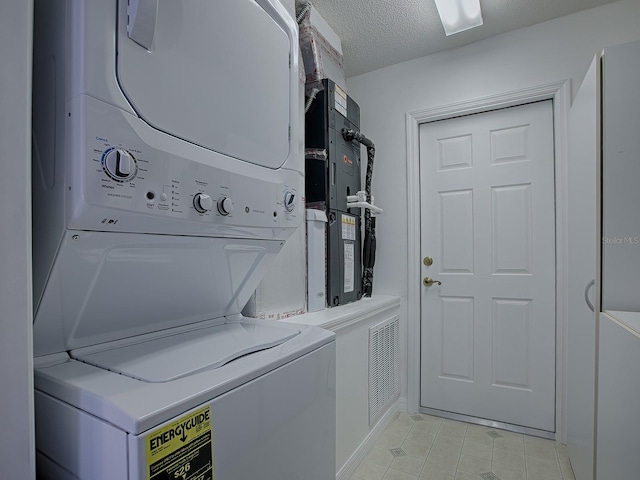 laundry area featuring a textured ceiling and stacked washer / drying machine