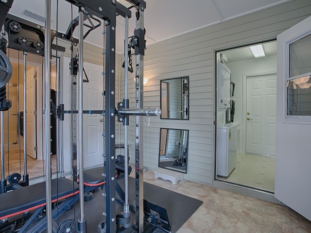 workout room with stacked washer and dryer and wooden walls