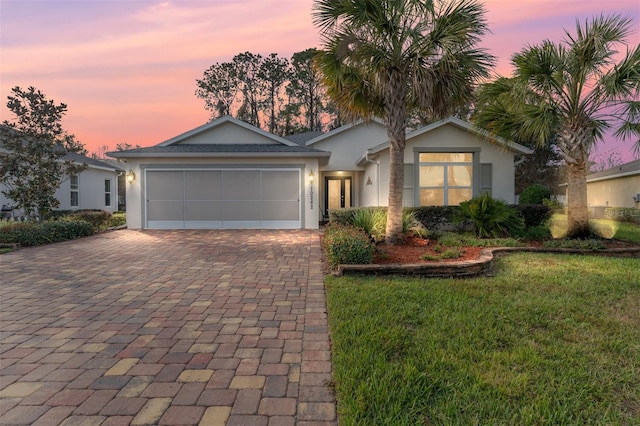 ranch-style house with a garage, decorative driveway, a lawn, and stucco siding