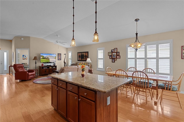 kitchen with a center island, vaulted ceiling, ceiling fan, decorative light fixtures, and light stone counters