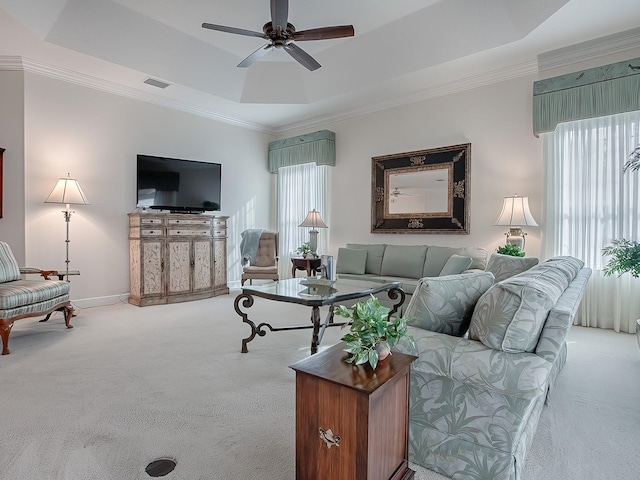 carpeted living room with baseboards, visible vents, a raised ceiling, ceiling fan, and crown molding