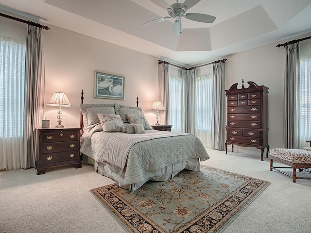 bedroom with a ceiling fan, a tray ceiling, and light colored carpet