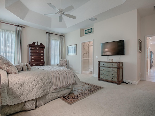 carpeted bedroom with a raised ceiling, ensuite bathroom, and ceiling fan