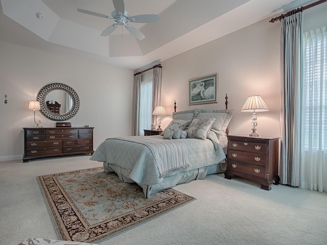 carpeted bedroom featuring ceiling fan, a raised ceiling, and multiple windows