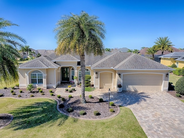 single story home with a garage, decorative driveway, a front lawn, and stucco siding