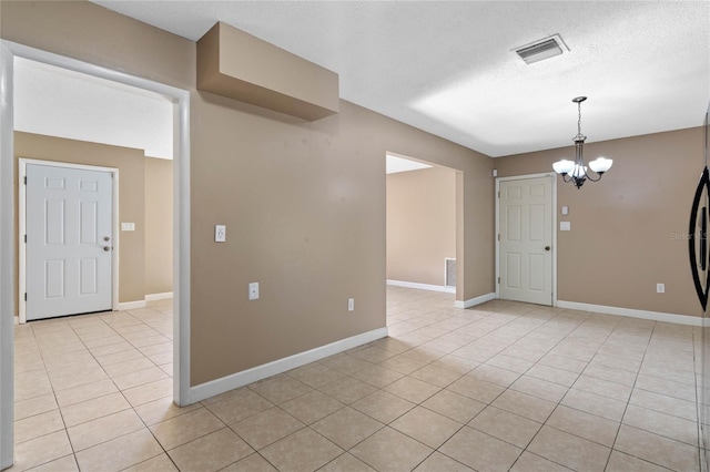 tiled spare room with a chandelier and a textured ceiling