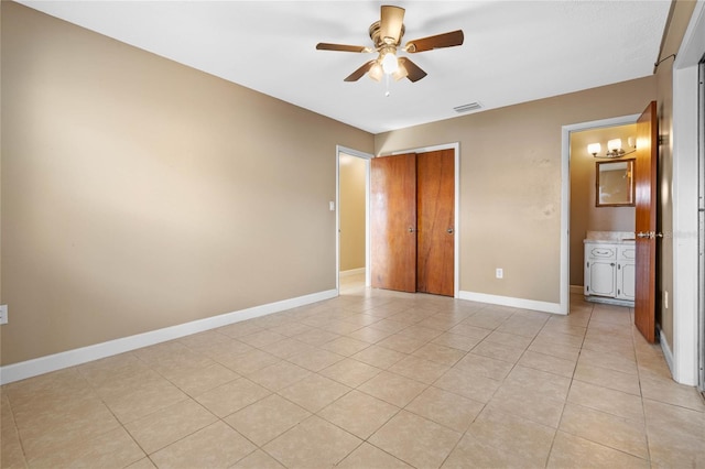 unfurnished bedroom featuring light tile patterned floors, a closet, ensuite bathroom, and ceiling fan