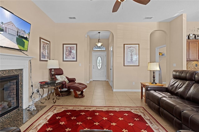 tiled living room with ceiling fan and a fireplace