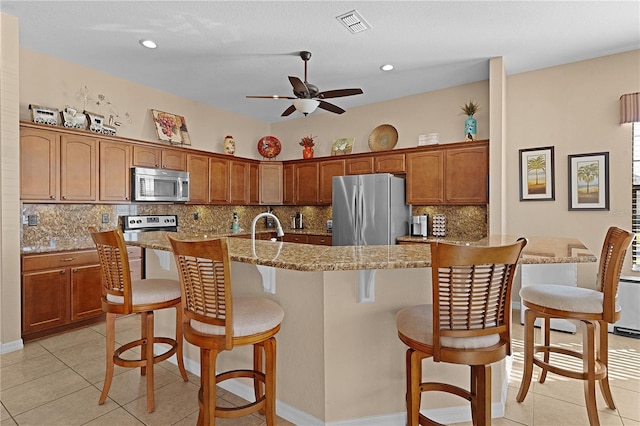 kitchen featuring a kitchen bar, light stone countertops, light tile patterned floors, and appliances with stainless steel finishes