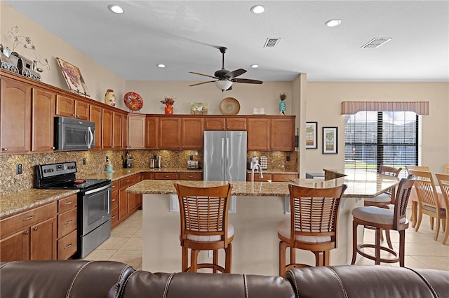 kitchen featuring light stone countertops, a kitchen breakfast bar, stainless steel appliances, and light tile patterned flooring